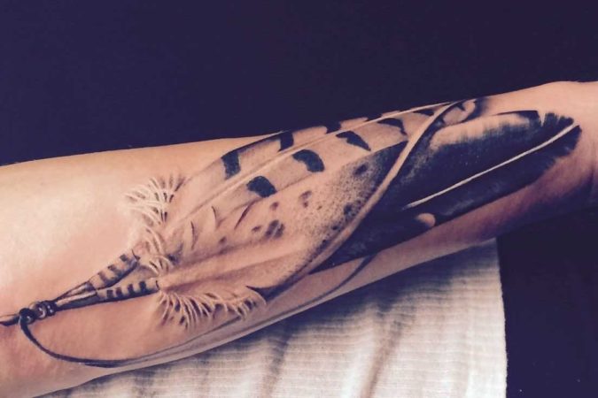 Tattoo of a feather on his forearm