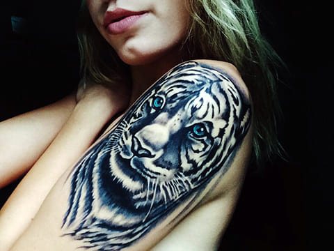 Tattoo of a tiger with blue eyes on a girl's shoulder