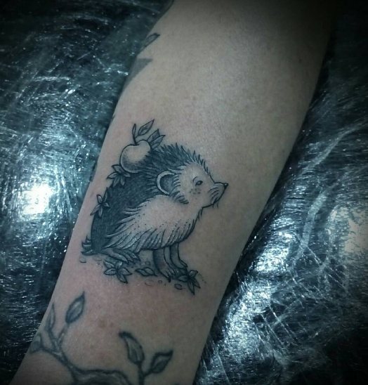 Tattoo of a hedgehog with an apple on his forearm